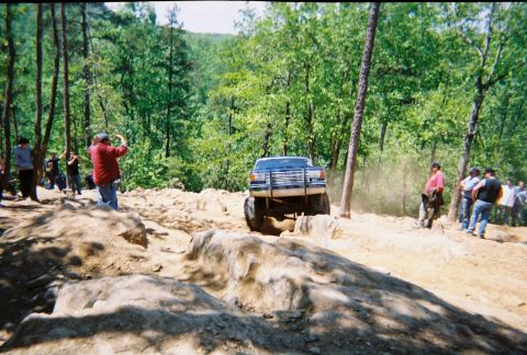 1988 Ford Bronco - Off-road vehicle tackling a challenging rocky path in a wooded area.