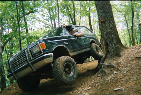 1988 Ford Bronco - A Ford Bronco navigates a challenging off-road course through a wooded area.