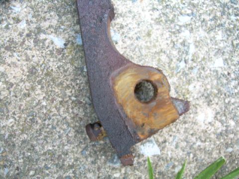 1988 Ford Bronco - A close-up view of a heavily rusted metal bracket, likely a vehicle part, situated on a textured concrete background.
