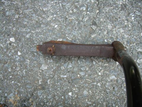 1988 Ford Bronco - Close-up of a corroded metal linkage component, likely for a vehicle's drivetrain, on a gravel surface.