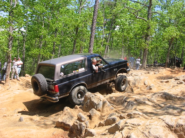 Dark blue Ford Bronco climbing rocks with front wheel in the air, spectators watching