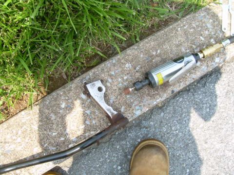 1988 Ford Bronco - A metal linkage part and a die grinder are shown on a concrete surface next to grass.