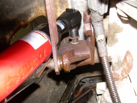 1988 Ford Bronco - Tight underside shot of a rusty cast bracket and bolt being turned with a black-handled ratcheting wrench, with a red Husky-branded tool ha…