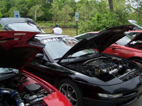 1995 Ford Probe - Multiple cars are parked with hoods open at an outdoor event, including a black 1995 Ford Probe.