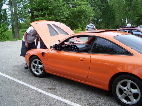 1995 Ford Probe - A person looks at the engine of an orange 1995 Ford Probe coupe parked outdoors.