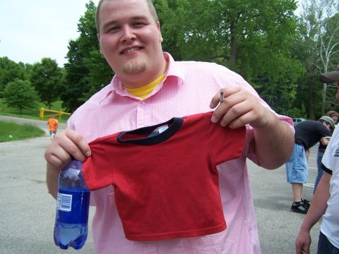 1995 Ford Probe - A man holds up a red t-shirt and a bottle of water while standing outdoors with other people and vehicles visible.