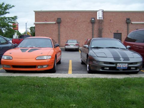 1995 Ford Probe - Two sporty coupes, an orange Mazda and a gray Ford, are parked in a lot.