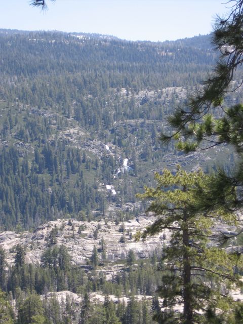 1994 Ford Bronco - A scenic view of a mountainous region covered in evergreen trees, with a small waterfall cascading down a rocky slope in the distance.