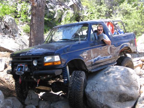 1994 Ford Bronco - A blue Ford Bronco navigates a rocky off-road course, demonstrating its capabilities on challenging terrain.