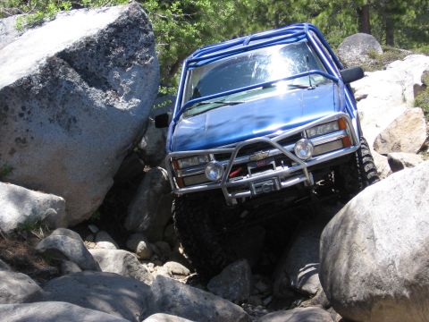 1994 Ford Bronco - A blue off-road vehicle with a roll cage and brush guard is shown navigating a rocky terrain.