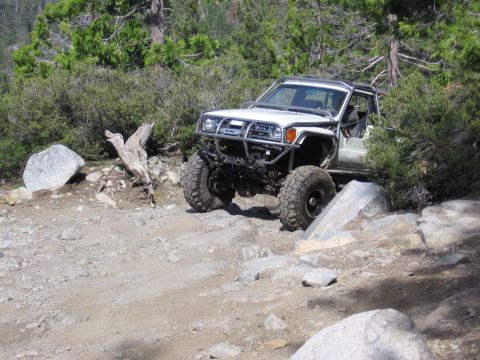1994 Ford Bronco - Modified SUV tackles a challenging off-road course with large boulders and dense foliage.
