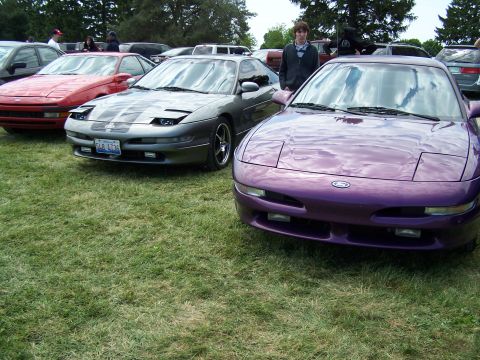 1995 Ford Probe - Several Ford Probes are gathered on a grassy field, with a young man standing between two of them.