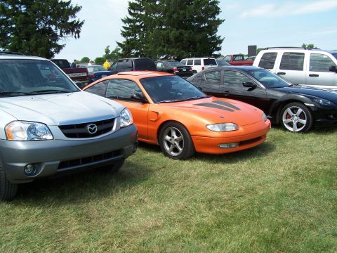 1995 Ford Probe - An orange Mazda MX-6 is parked on grass next to other vehicles.