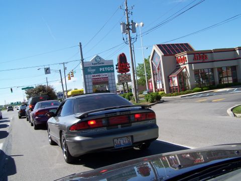 1995 Ford Probe - A line of cars, including a gray coupe, waits in traffic near a shopping center and Arby's.