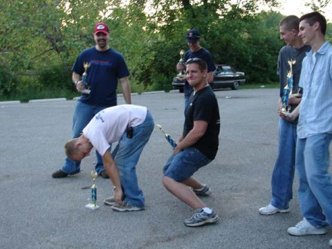 1995 Ford Probe - Several men are gathered around trophies, with a vintage black car in the background.