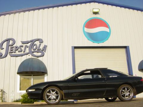 1995 Ford Probe - Side view of a black 1995 Ford Probe GT parked in front of a Pepsi building.