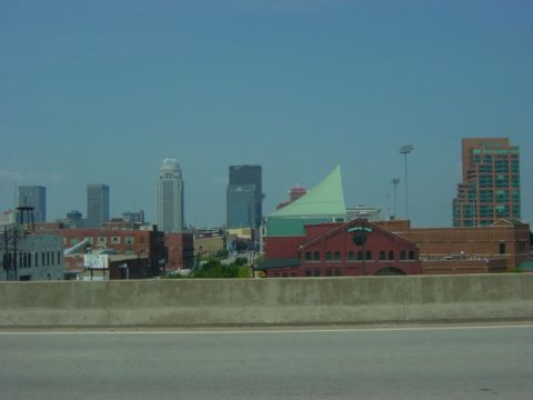1995 Ford Probe - A view of a city skyline is seen from a highway, with a concrete barrier in the foreground and a clear blue sky above.