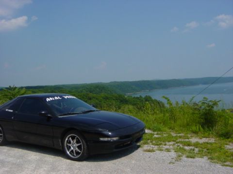 1995 Ford Probe - A black 1995 Ford Probe is parked on a scenic overlook with a lake and trees in the background.