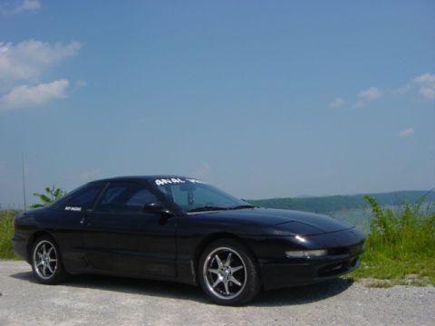 1995 Ford Probe - A black 1995 Ford Probe is parked outdoors near a body of water under a blue sky.