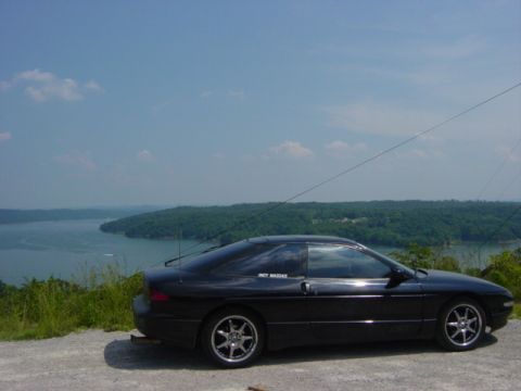 1995 Ford Probe - A black 1995 Ford Probe is parked on a scenic overlook with a lake and trees visible.