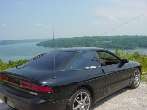 1995 Ford Probe - A black Mazda MX-6 coupe is parked overlooking a large body of water on a sunny day.