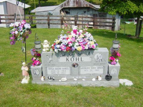 1995 Ford Probe - A memorial scene a gravestone adorned with flowers, set in a grassy outdoor area with a rustic building in the background.