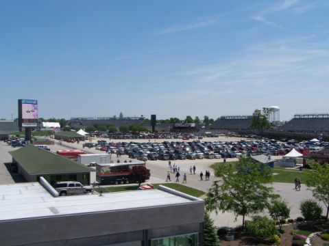 1995 Ford Probe - A vast parking area is filled with numerous vehicles, set against the backdrop of a stadium and a water tower on a sunny day.