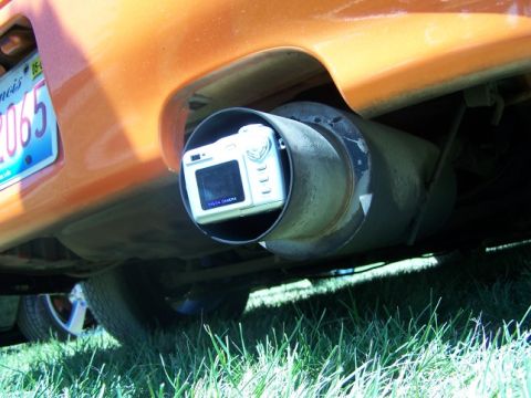 1995 Ford Probe - A digital camera is placed inside the exhaust pipe of an orange vehicle, with a license plate visible.