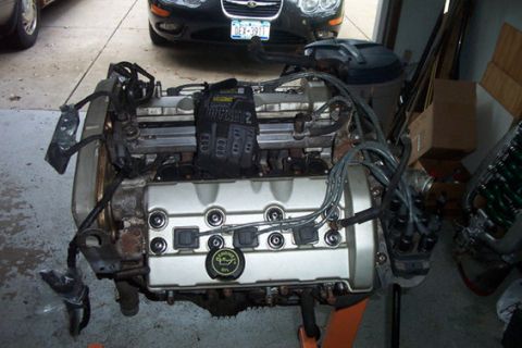1995 Ford Taurus - Engine assembly on a stand, with black work gloves placed on top of the valve cover.
