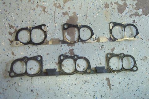 1995 Ford Taurus - Several engine intake manifold gaskets are laid out on a speckled concrete floor, showing their dual-port design.