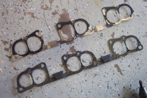 1995 Ford Taurus - Four exhaust manifold gaskets are laid out on a speckled concrete floor.