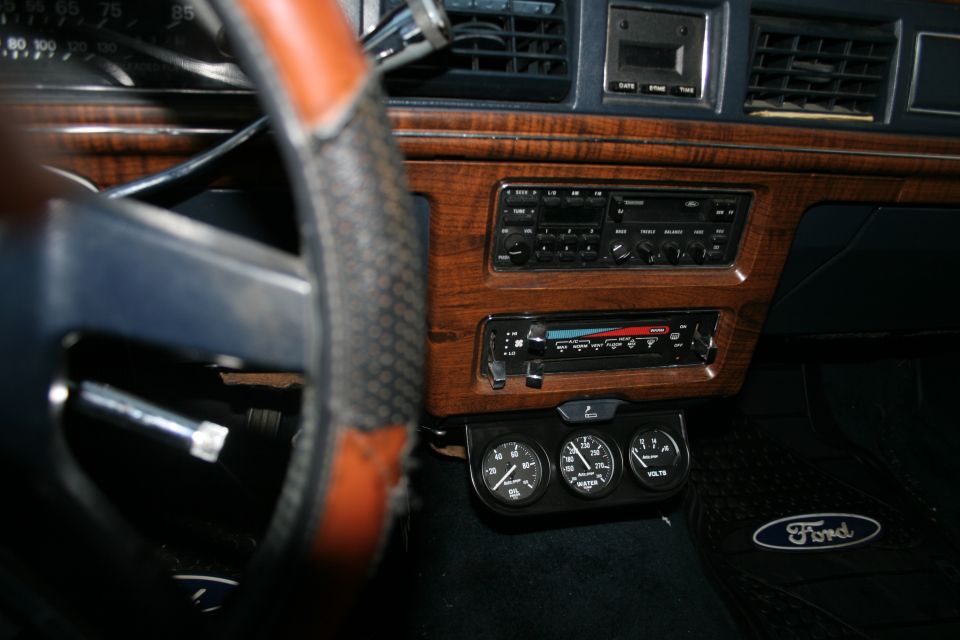 Dashboard of a 1989 Ford Crown Victoria LTD with wood grain trim, aftermarket gauges, and a Ford floor mat