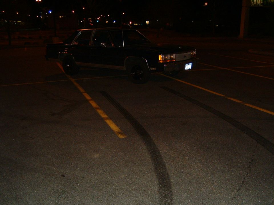 Black Ford Crown Victoria parked at night with tire marks on the asphalt