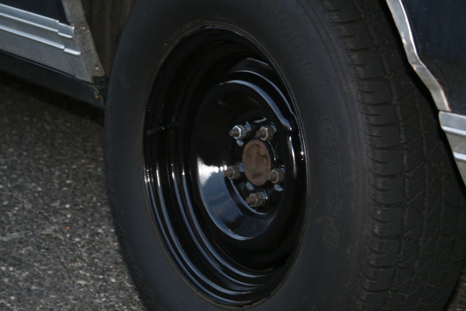Black steel wheel with five lug nuts on a car tire. Chrome trim visible on the car body