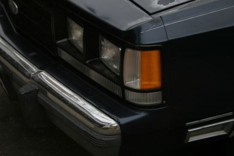 1989 Ford Crown Victoria LTD - Close-up of the front corner of a dark sedan, highlighting the headlight assembly and chrome bumper details.