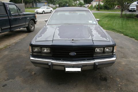 1989 Ford Crown Victoria LTD - A dark blue Ford Crown Victoria with peeling paint sits in a driveway, parked next to a dark green pickup truck.