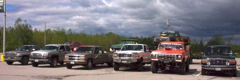 1978 Ford Bronco - A collection of modified pickup trucks are parked together under a cloudy sky.
