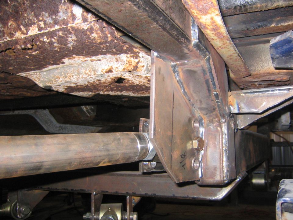 Close-up of custom metal fabrication on a vehicle's undercarriage, showing welded brackets and a large pipe