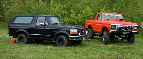 1978 Ford Bronco - A black Ford Bronco and a lifted orange pickup truck are parked side-by-side on a grassy field.