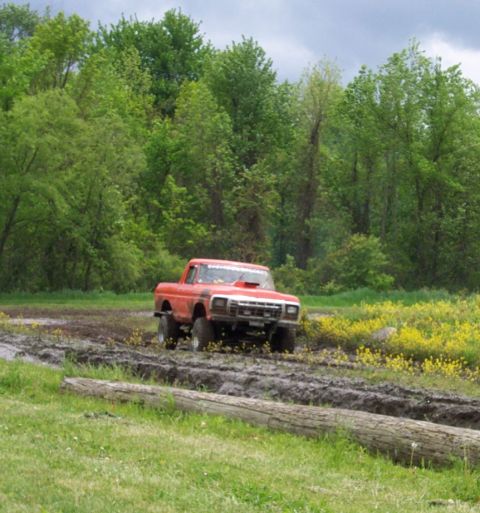 1978 Ford Bronco - A red 1979 Ford F-Series pickup truck navigates a muddy track surrounded by lush greenery and yellow wildflowers.