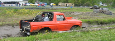 1978 Ford Bronco - An orange off-road truck is stuck in a mud pit, with another vehicle visible in the background.