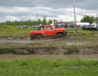 1978 Ford Bronco - An orange pickup truck navigates through a muddy field under a cloudy sky.
