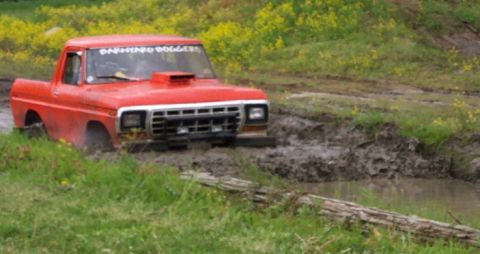 1978 Ford Bronco - This red 1979 Ford F-Series pickup truck, a hood scoop and "BARNHARD DOGGERS" text on the windshield, is stuck in a muddy off-road course.