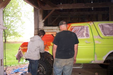 1978 Ford Bronco - Two individuals are working on the body of a 1978 Ford Bronco, which is undergoing preparation for a new paint job.