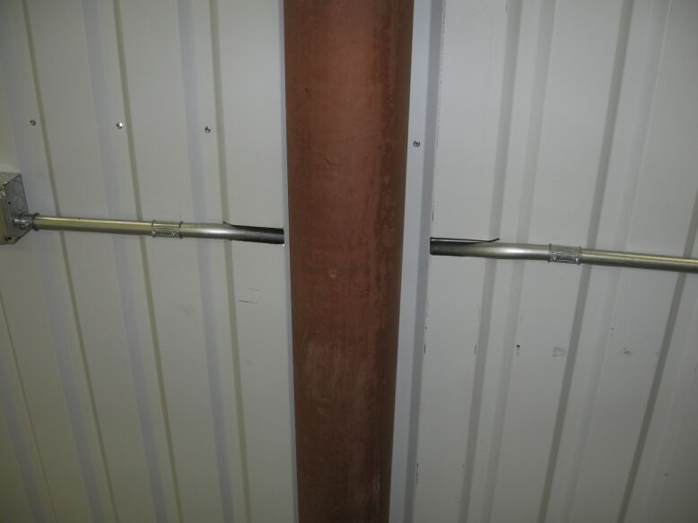 Shop wall with white metal paneling, rust-colored post and galvanized electrical conduit