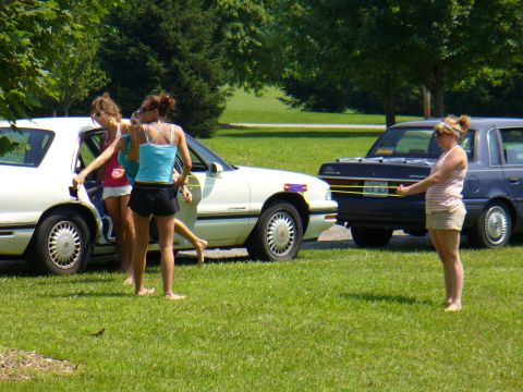 1991 Ford Probe - Three young women are gathered around a white sedan, while another car is parked behind it.