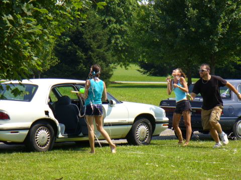1991 Ford Probe - A group of people engage in a water gun fight next to two parked cars on a sunny day.
