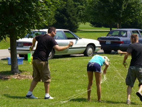 1991 Ford Probe - Two cars are parked in the background while people engage in a water gun fight on a sunny day.