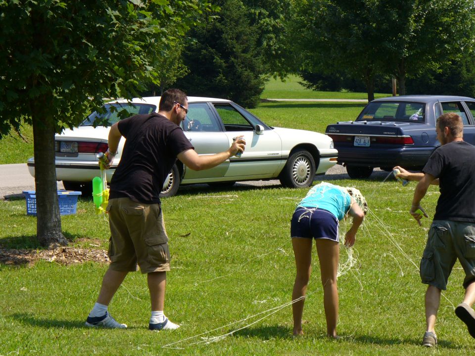 People having a water gun fight in a park with two cars in the background