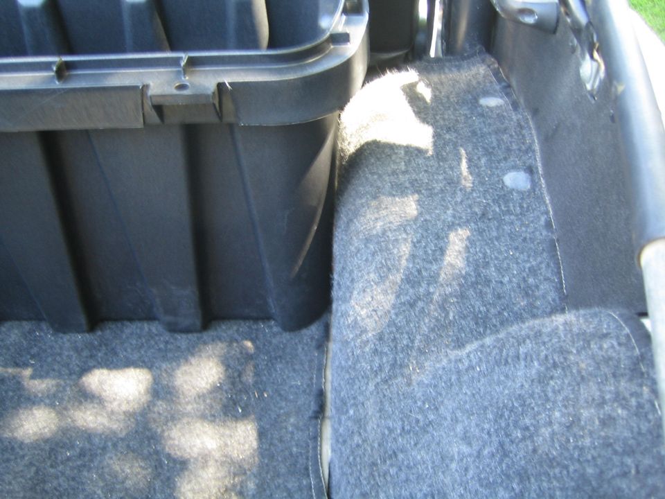 Interior view of a black storage bin next to a grey carpeted panel in a vehicle